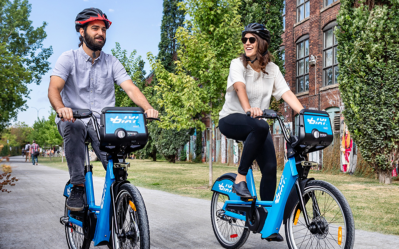 Transport urbain partagé - Homme et femme portant des casques se promènent en vélo partage Bixi